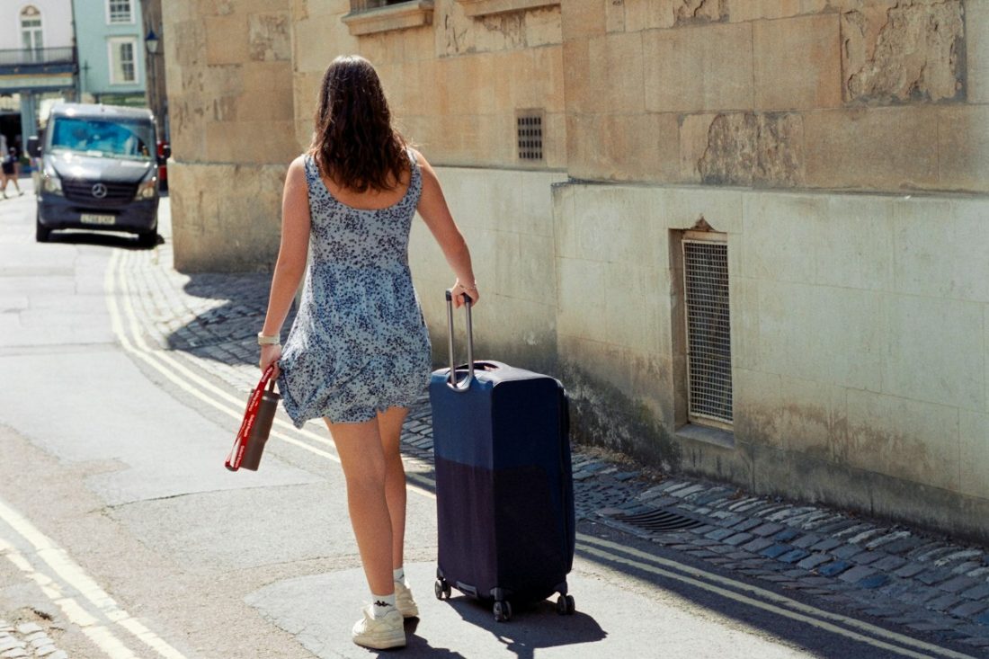 Woman pulling a suitcase along a sunny stone street after moving abroad